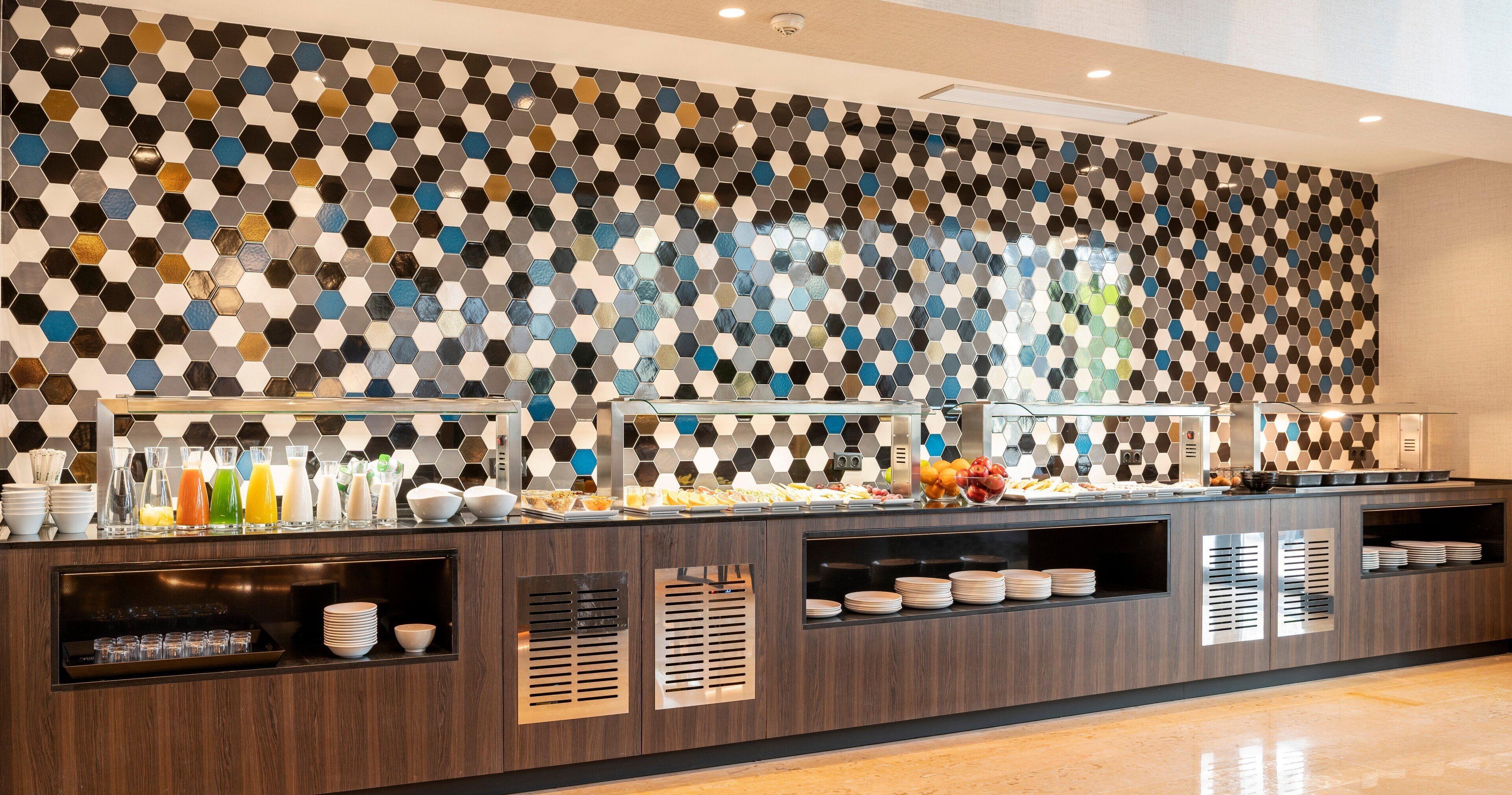 A buffet area with a patterned wall, a variety of food items, and a selection of beverages.