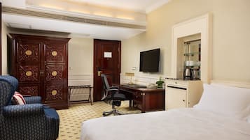 A hotel room with a bed, a desk with a chair, a television, and a wardrobe.