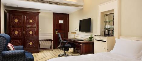 Quarto de hotel com uma cama, uma escrivaninha com cadeira, uma televisão e um guarda-roupa.