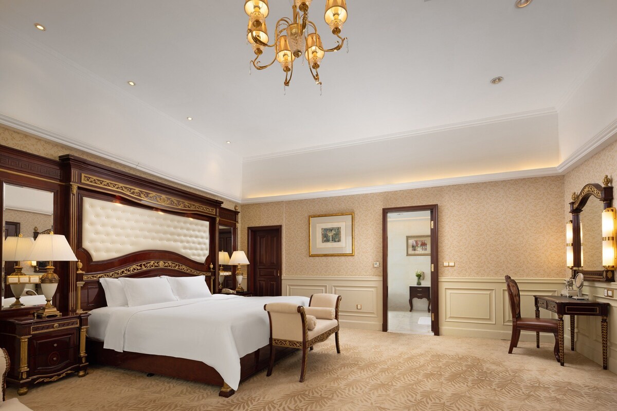 Une chambre d’hôtel luxueuse, dotée d’un grand lit, d’un coin salon et d’un bureau avec un miroir.