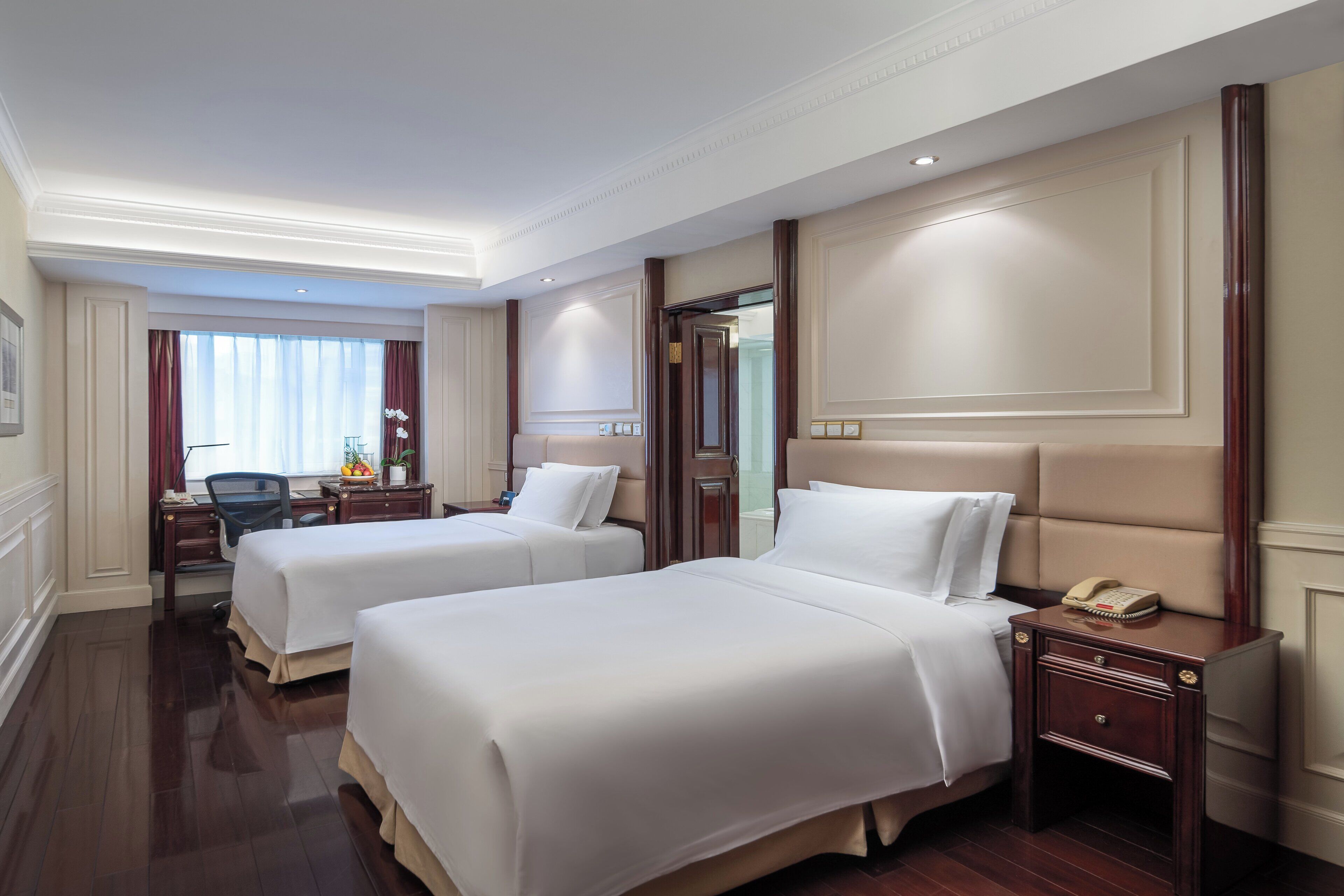 A hotel room with two beds, a desk, a chair, and a nightstand with a telephone.