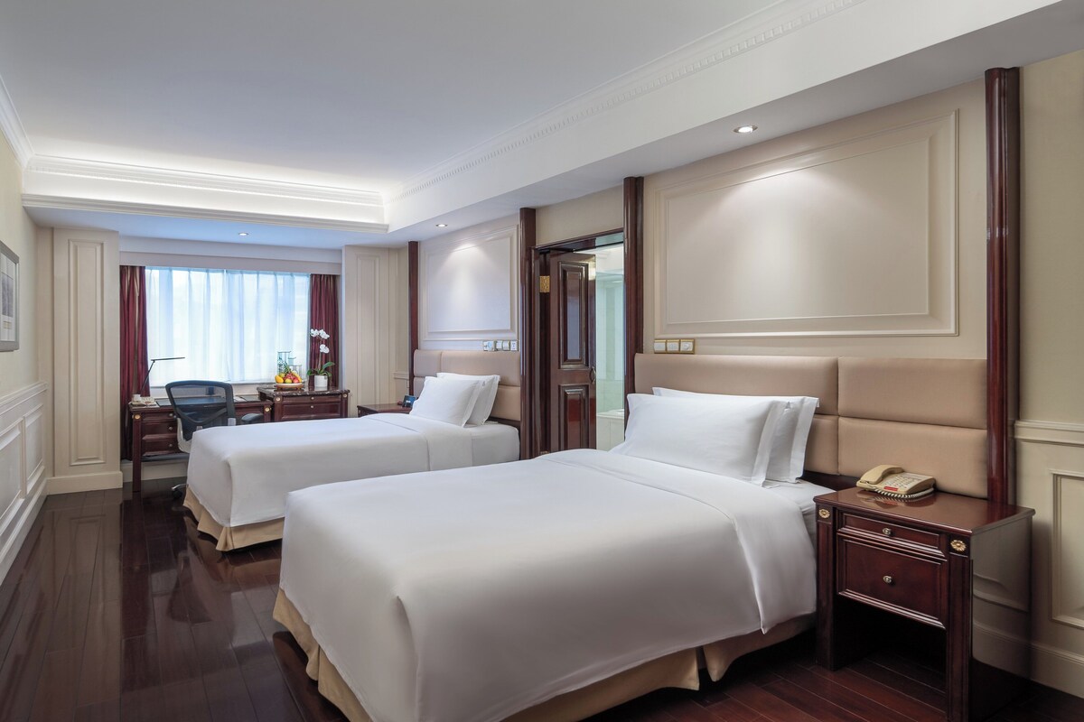 Une chambre d’hôtel avec deux lits, un bureau, une chaise et une table de chevet avec un téléphone.