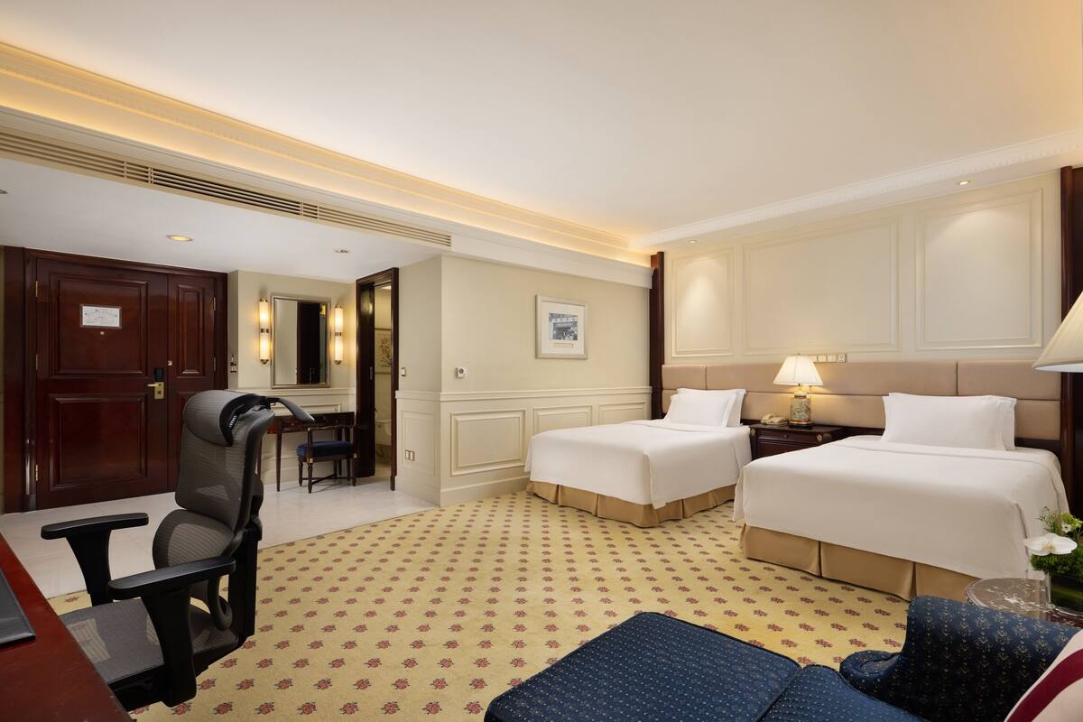 Ein Hotelzimmer mit zwei Betten, einem Schreibtisch, einem Sessel und einer Couch.