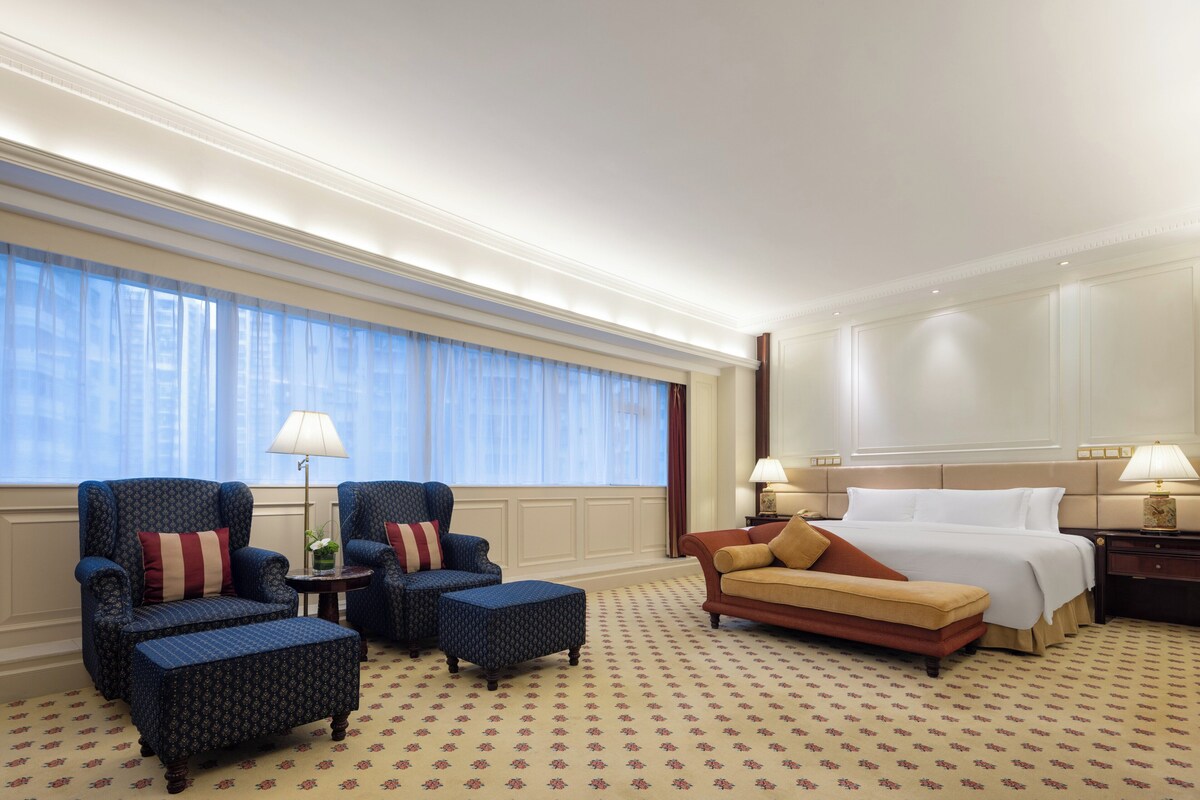 Une chambre d’hôtel avec un grand lit, deux fauteuils, un canapé, une petite table et une table de chevet.