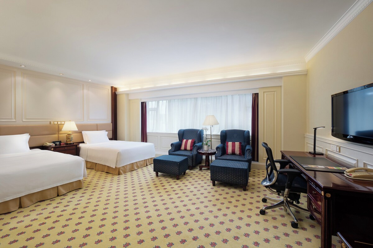 Une chambre d’hôtel avec deux lits, un bureau, une télévision et une fenêtre avec des rideaux.