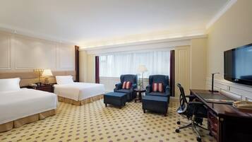A hotel room with two beds, a desk, a television, and a window with curtains.