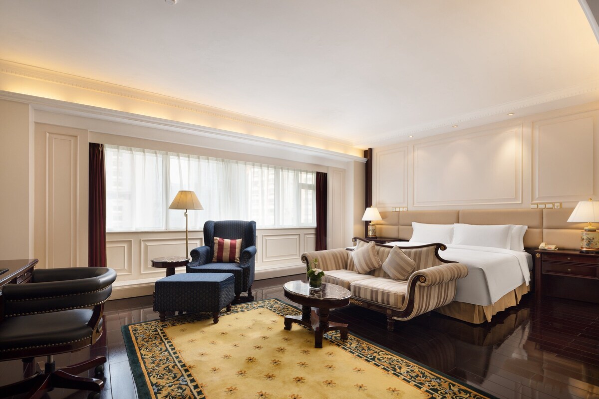 Une chambre d’hôtel spacieuse, dotée d’un grand lit, d’un canapé, d’un fauteuil, d’un bureau et d’une petite table.