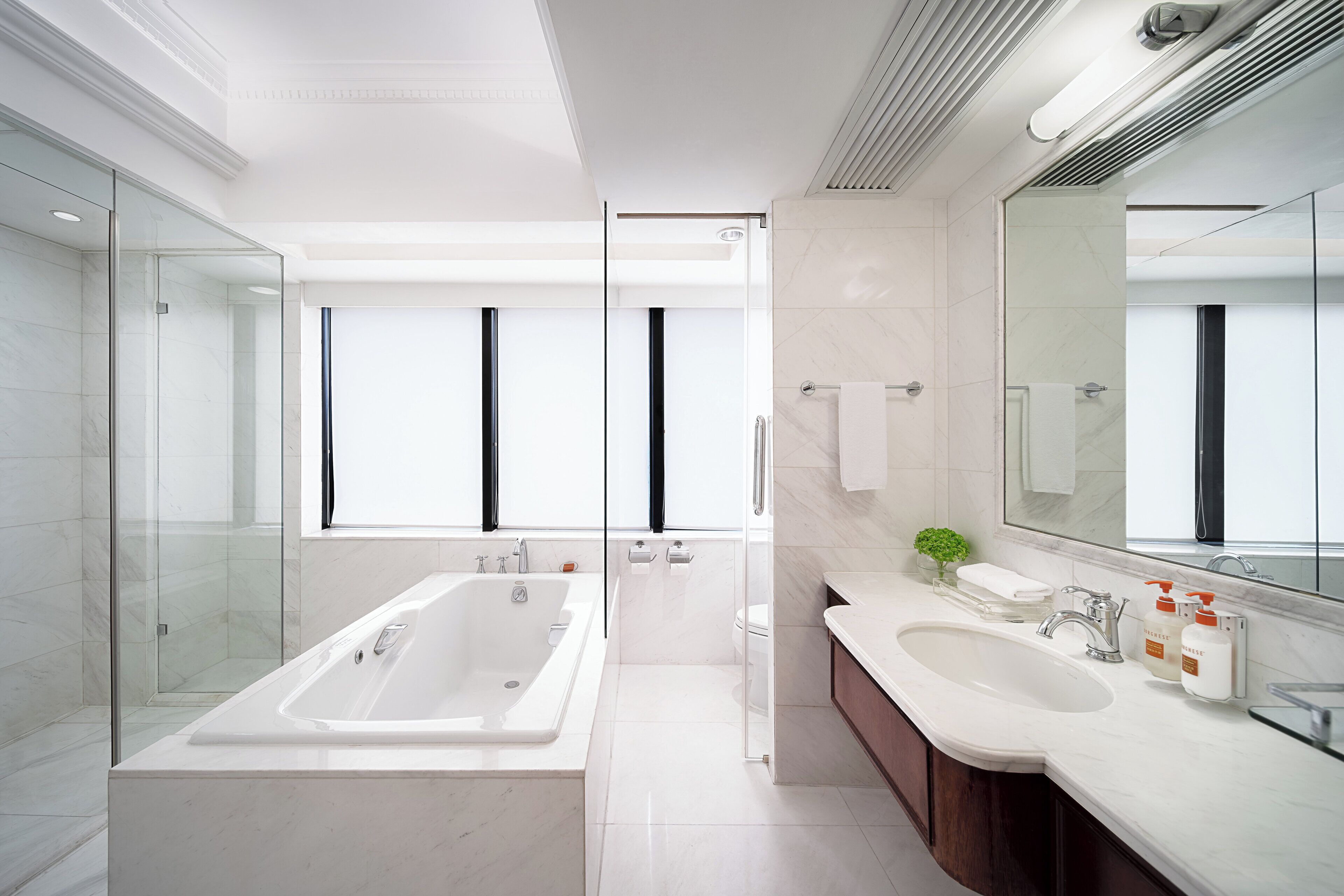 A modern bathroom with a glass-enclosed shower, a freestanding bathtub, a vanity with a large mirror, and a toilet.