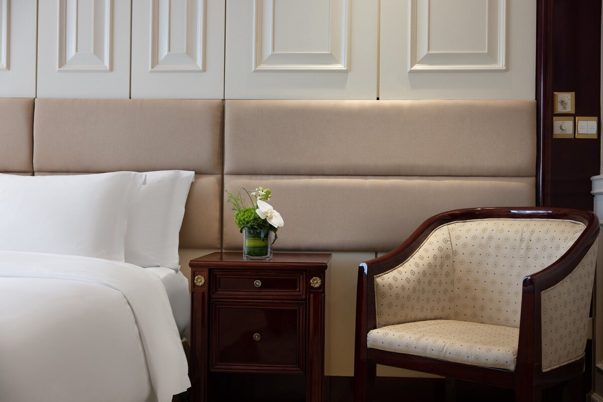 Une chambre d’hôtel comprenant un lit, une table de chevet, une chaise et un vase décoratif avec des fleurs.