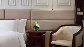 A hotel room with a bed, a nightstand, a chair, and a decorative vase with flowers.