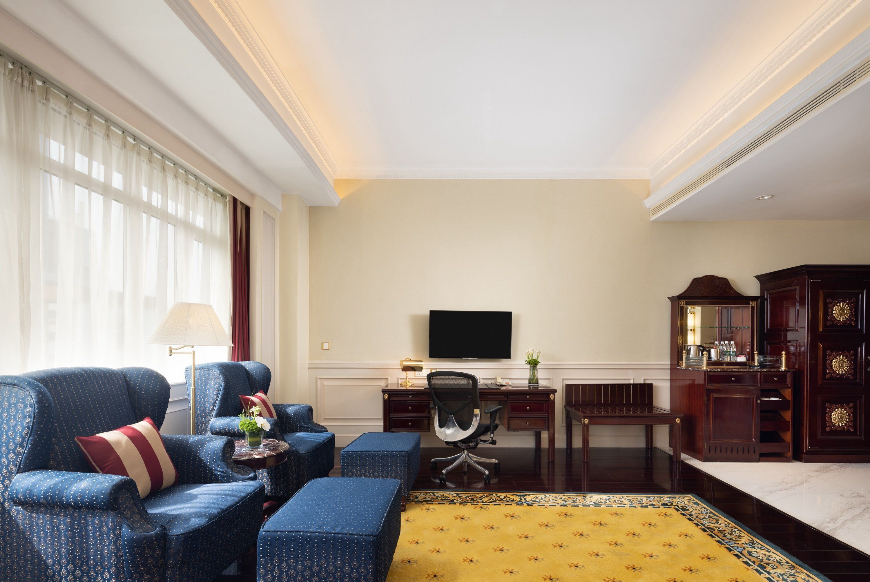 A hotel room with a sofa, a desk, a television, and a cabinet.