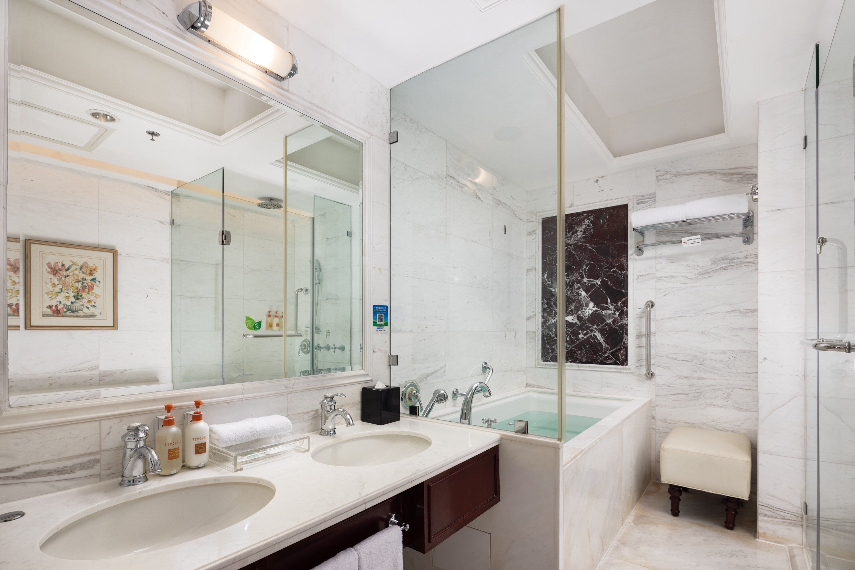 A modern bathroom with two sinks, a large mirror, a glass shower enclosure, and a marble-tiled wall.
