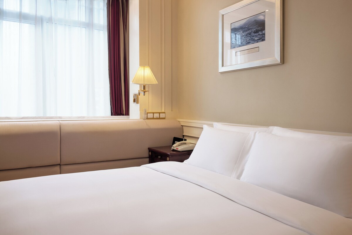 Une chambre d’hôtel avec un lit, une table de chevet avec une lampe, un téléphone et un tableau encadré au mur.