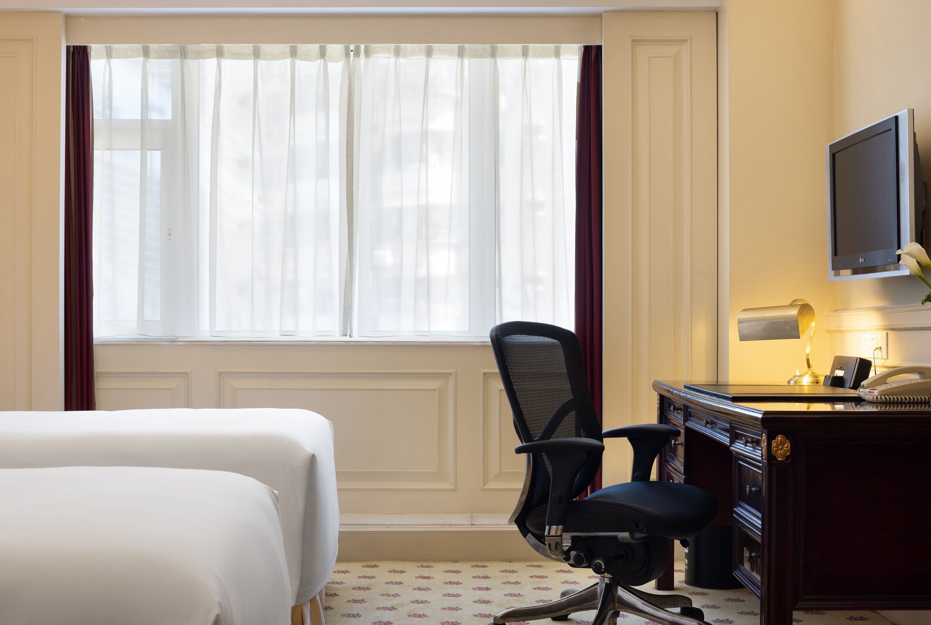 A hotel room with a bed, a desk with a computer, a chair, and a television.
