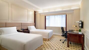 Une chambre d’hôtel avec deux lits, un bureau, une chaise et une fenêtre avec des rideaux.