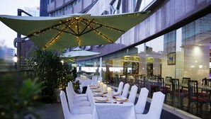 Een terras met tafels gedekt voor een maaltijd, omringd door potplanten en parasols.