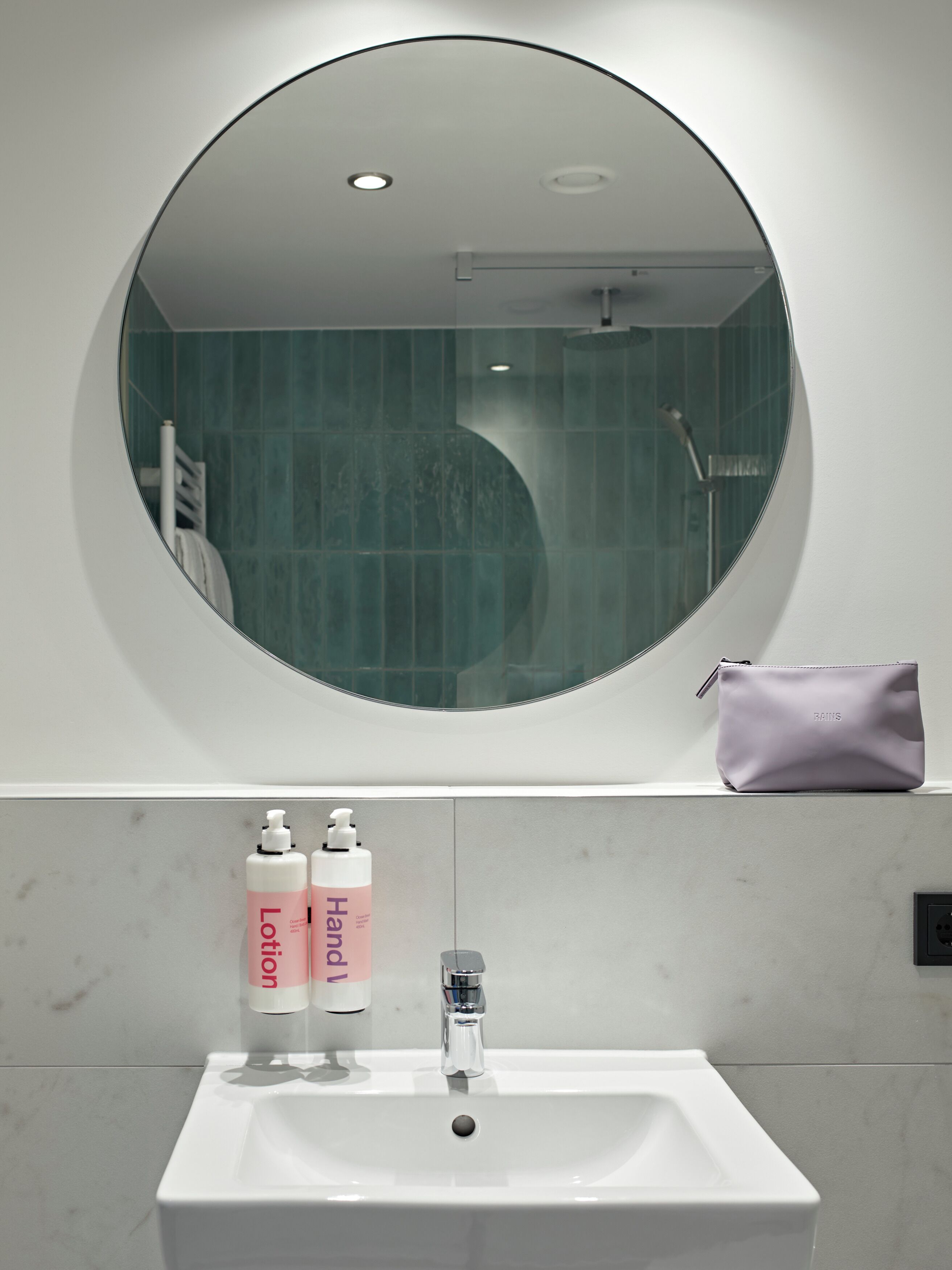 Een badkamer met een ronde spiegel, een wastafel en twee flesjes lotion.
