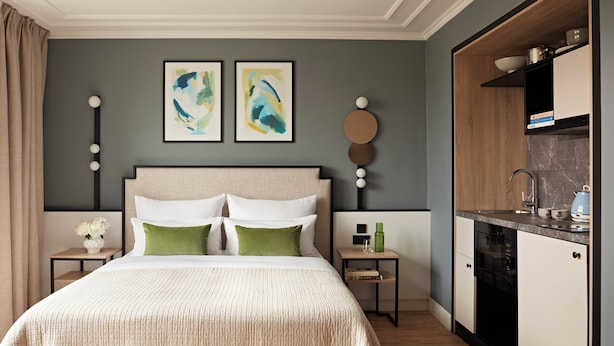 A modern bedroom with a large bed, a bedside table with a vase of flowers, and a small table with a green bottle and a glass. - Numa Berlin Checkpoint Charlie (Berlin)