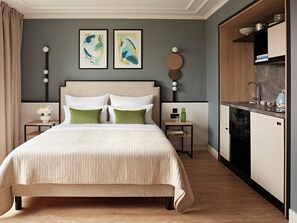 A modern bedroom with a large bed, a bedside table with a vase of flowers, and a small table with a green bottle and a glass. - Numa Berlin Checkpoint Charlie (Berlin)