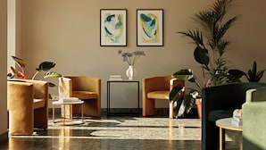 A modern lobby with two framed abstract paintings, a variety of seating options including a sofa and chairs, a small table with a vase of flowers, and several potted plants. - Numa Berlin Checkpoint Charlie (Berlin)