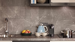 A modern kitchen with a marble backsplash, a built-in microwave, a kettle, a coffee maker, and a pot on the counter. - Numa Berlin Checkpoint Charlie (Berlin)