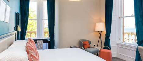 Habitación de hotel con una cama grande, un escritorio, una silla, una lámpara y vistas al exterior.