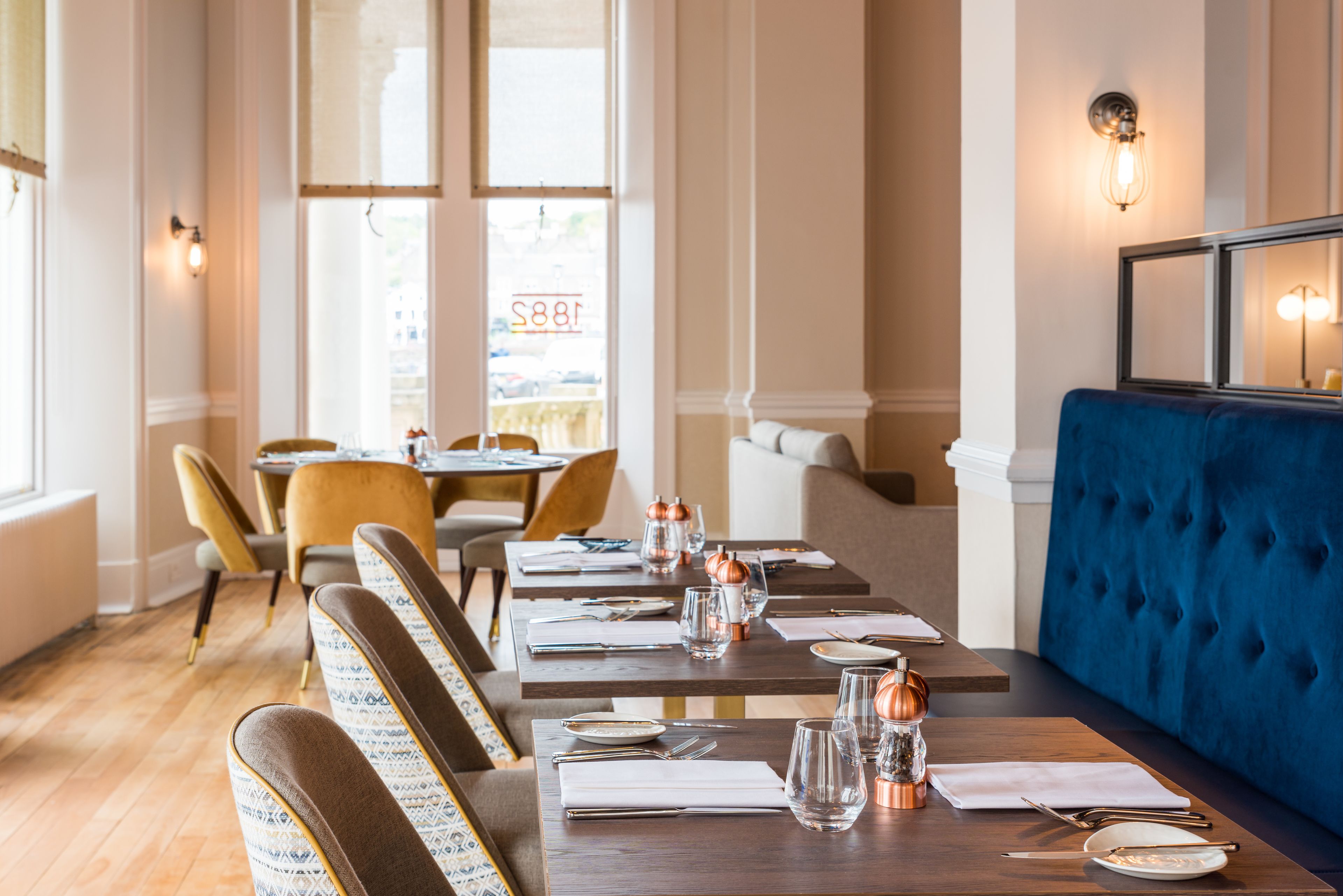 L’intérieur d’un restaurant avec des tables en bois, des chaises rembourrées et un banc recouvert d’un tissu bleu.
