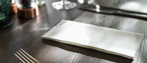 Una mesa de comedor con un mantel blanco, dos tenedores, un cuchillo y dos copas de vino.