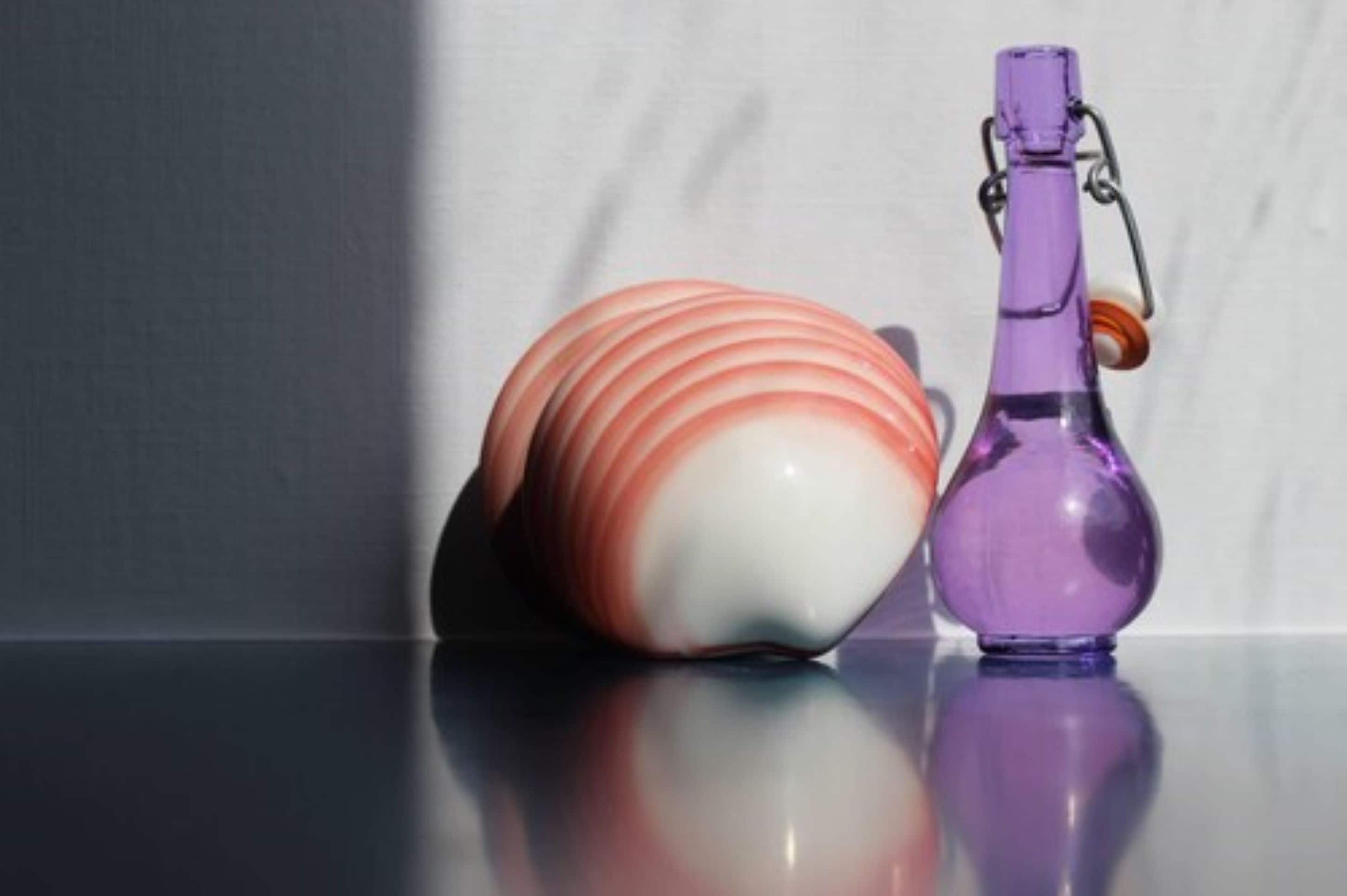 A decorative object with a purple bottle and a multicolored spherical item on a reflective surface.