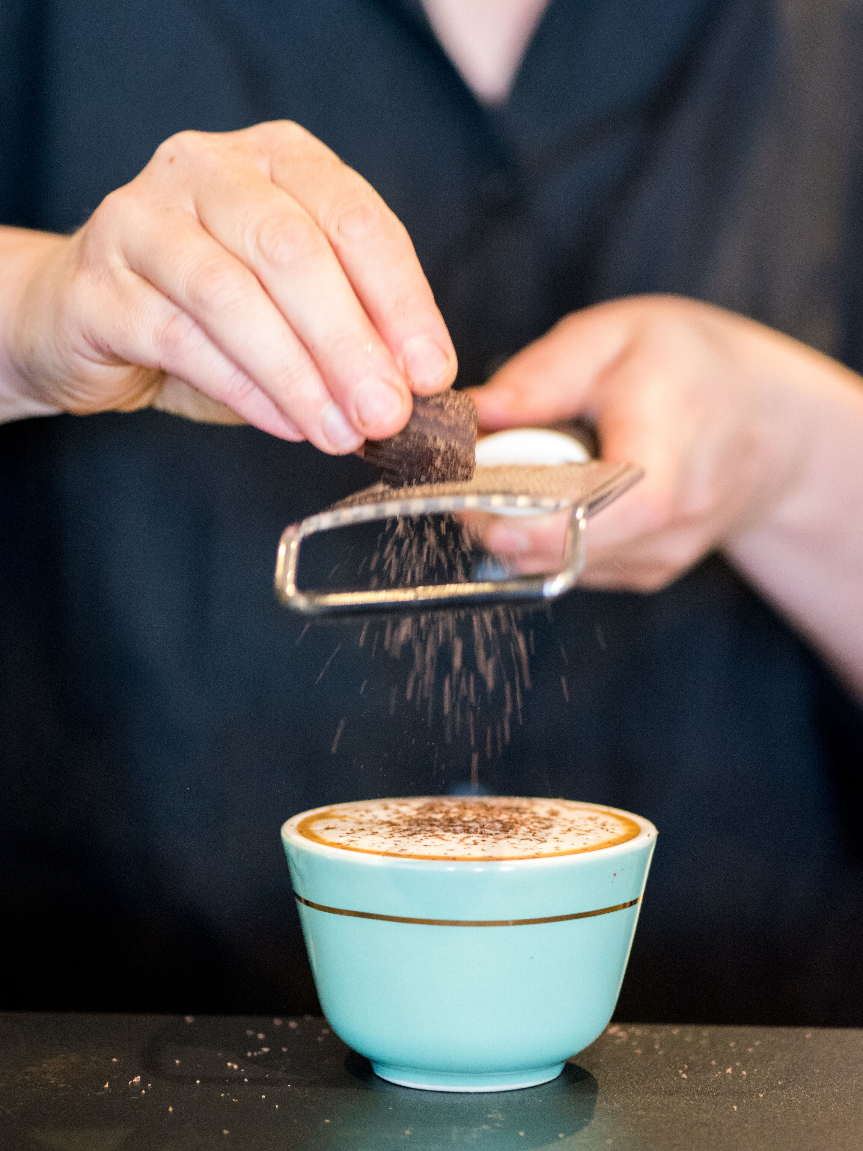 Eine Person streut eine pulverförmige Substanz in eine hellblaue Tasse mit goldener Kante.