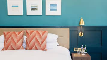 A neatly made bed with two orange pillows, a bedside table with a lamp, and three framed pictures on the wall.