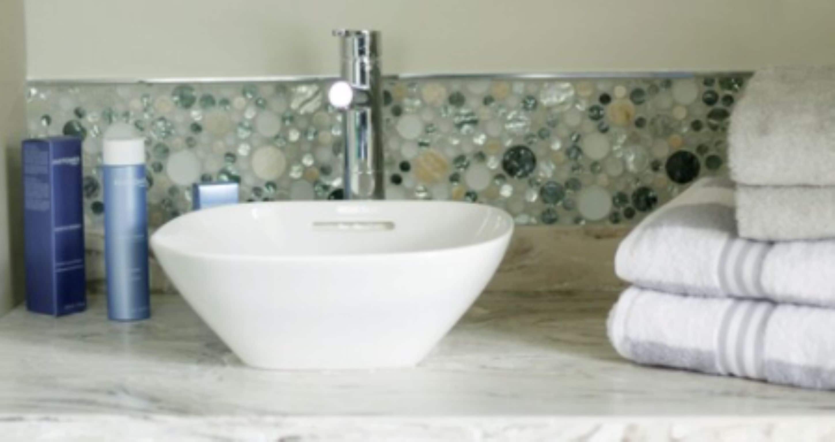 A bathroom with a white sink, a mirror, and a mosaic tile backsplash.