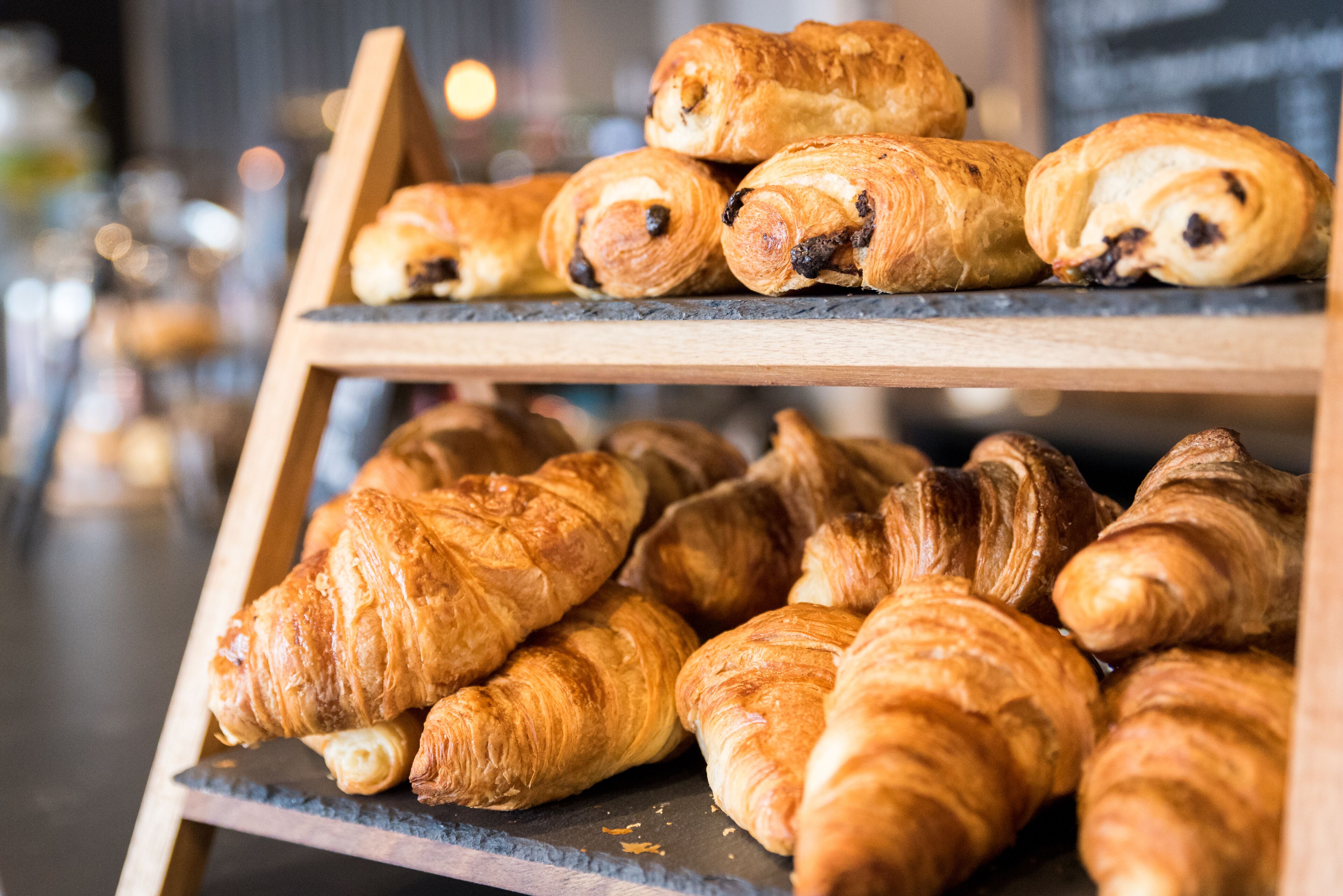 A display of assorted pastries, including croissants and chocolate-filled pastries, arranged on a wooden stand.