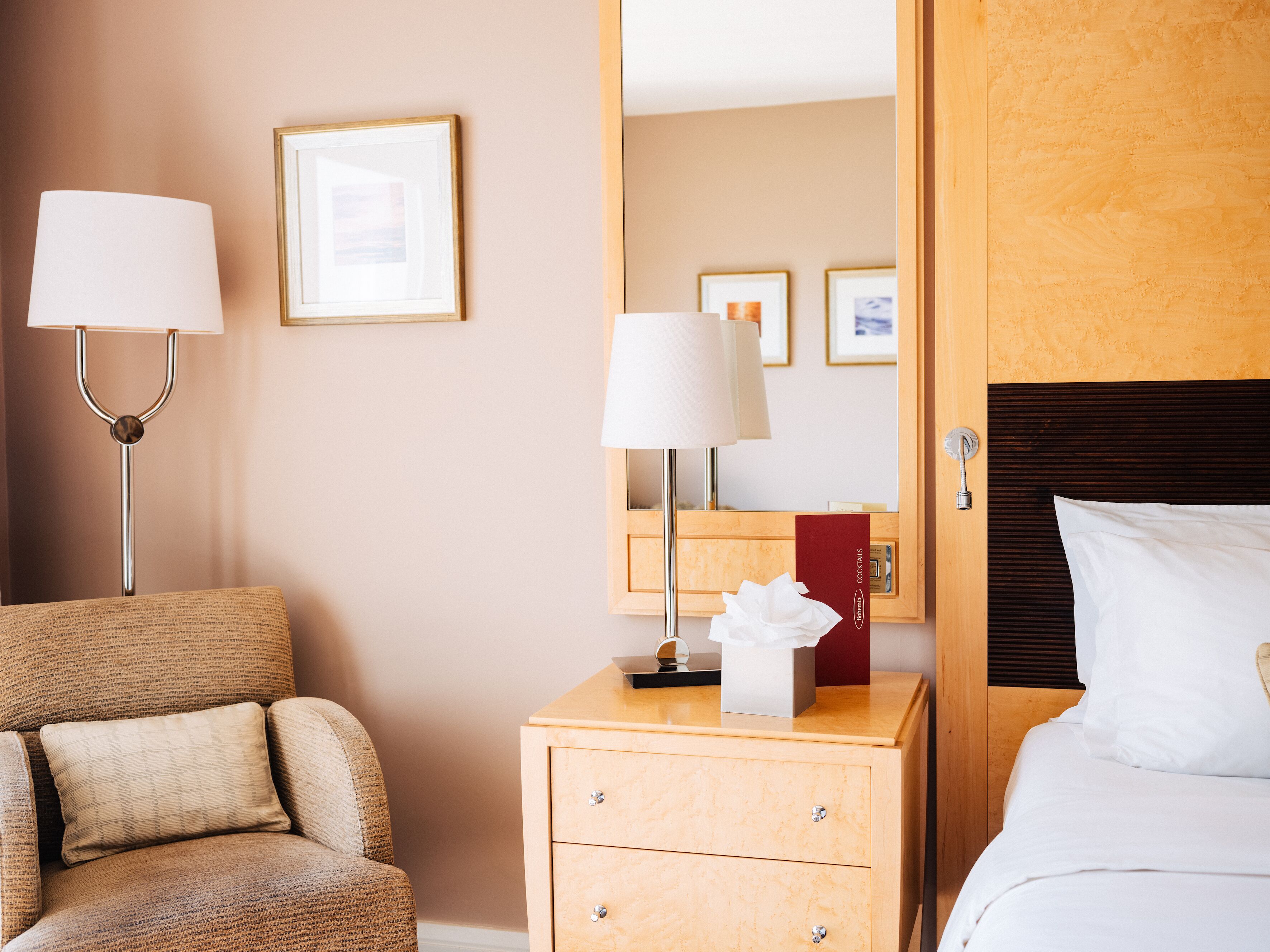 Una habitación de hotel con una cama, una mesita de noche con lámpara, una silla y un cabecero de madera.