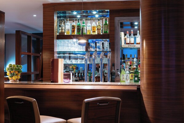 A bar area with a wooden counter, multiple liquor bottles, and two bar stools. - The Club Hotel and Spa (St. Helier)