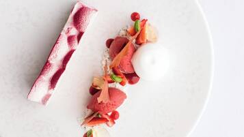 A dessert plate with a white plate and a dessert featuring red and white elements, garnished with small fruits and leaves.