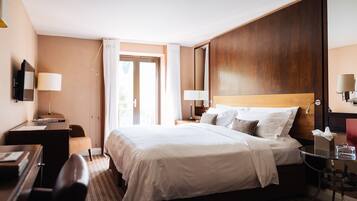 A hotel room with a large bed, a desk, a chair, a small table, and a mirror.