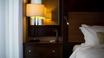 Een hotelkamer met een bed, nachtkastje met een lamp, spiegel en een houten hoofdeinde.