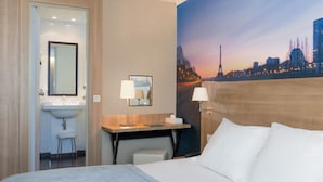 Habitación de hotel con cama, un escritorio y una silla, un lavamanos y un cuadro grande con una vista panorámica de la ciudad.