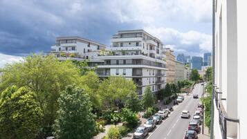 Un immeuble résidentiel à plusieurs étages, doté de balcons, avec des voitures garées et des arbres le long de la rue.