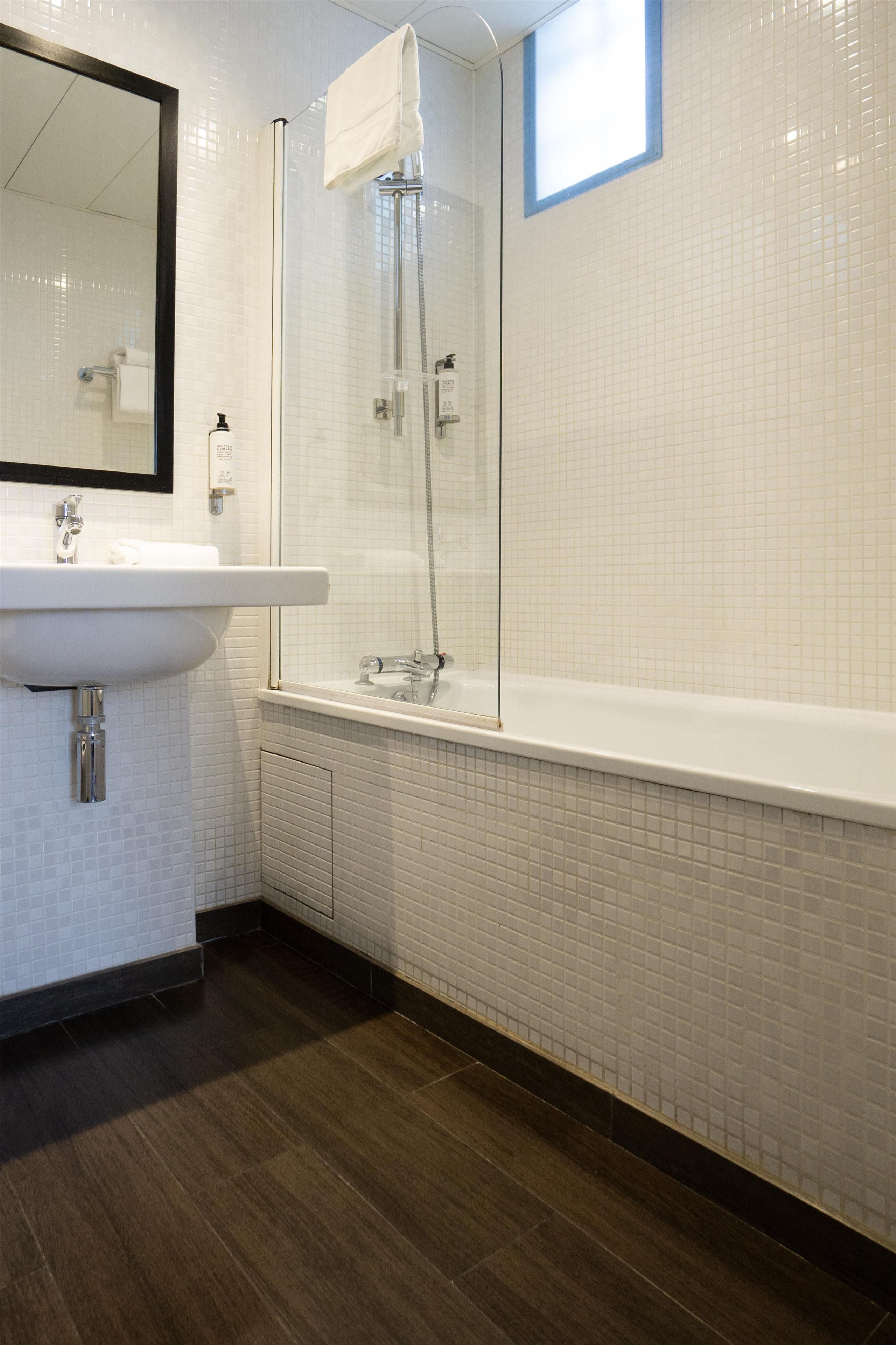 Un baño con lavamanos blanco, espejo y ducha con puerta de vidrio.