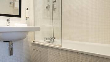 Un baño con lavamanos blanco, espejo y ducha con puerta de vidrio.