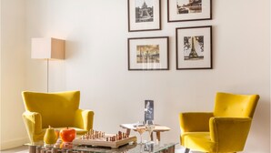 Una sala de estar moderna con dos sillones amarillos, una mesa de centro de vidrio con piezas de ajedrez y cuadros enmarcados en la pared.