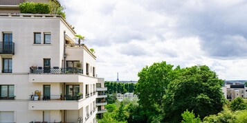 Un edificio residencial de varios pisos con balcones, vista a la Torre Eiffel y follaje circundante.