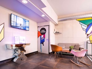 A modern lobby with a flat-screen TV, a couch, a coffee table, and a unique geometric wall art piece. - ibis Styles Paris Maine Montparnasse (Paris)