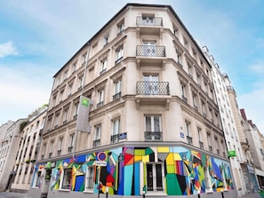 Un edificio en esquina con fachada colorida, un letrero que dice 'ibis Styles Hotel' y un cartel de 'prohibido estacionar'.