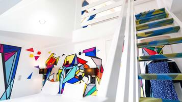 A modern interior with a staircase, geometric wall art, and a patterned fabric draped over the railing.