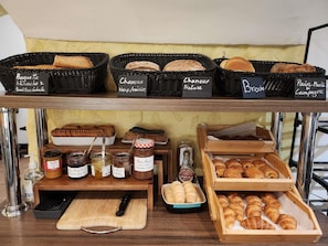 Een bakkerijdisplay met diverse broden en gebak, inclusief labels voor soorten zoals 'Baguette blanche & traditionale' en 'Choux Noix/Traisin'.