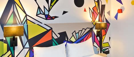 Une chambre d’hôtel avec un lit, deux lampes de chevet, un mur orné de motifs géométriques et une petite table ronde.