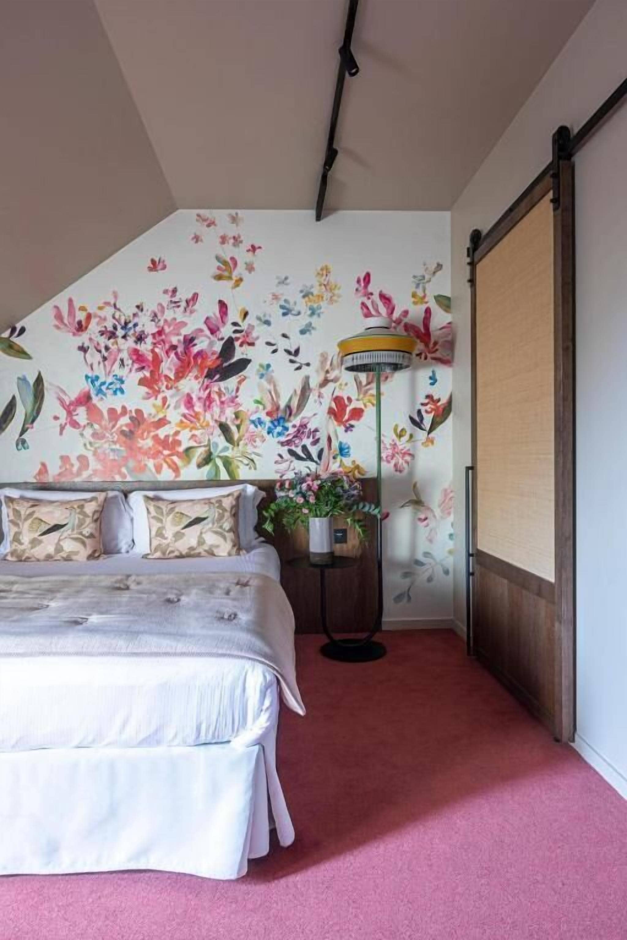 A bedroom with a bed, a potted plant, a floor lamp, and a sliding door.
